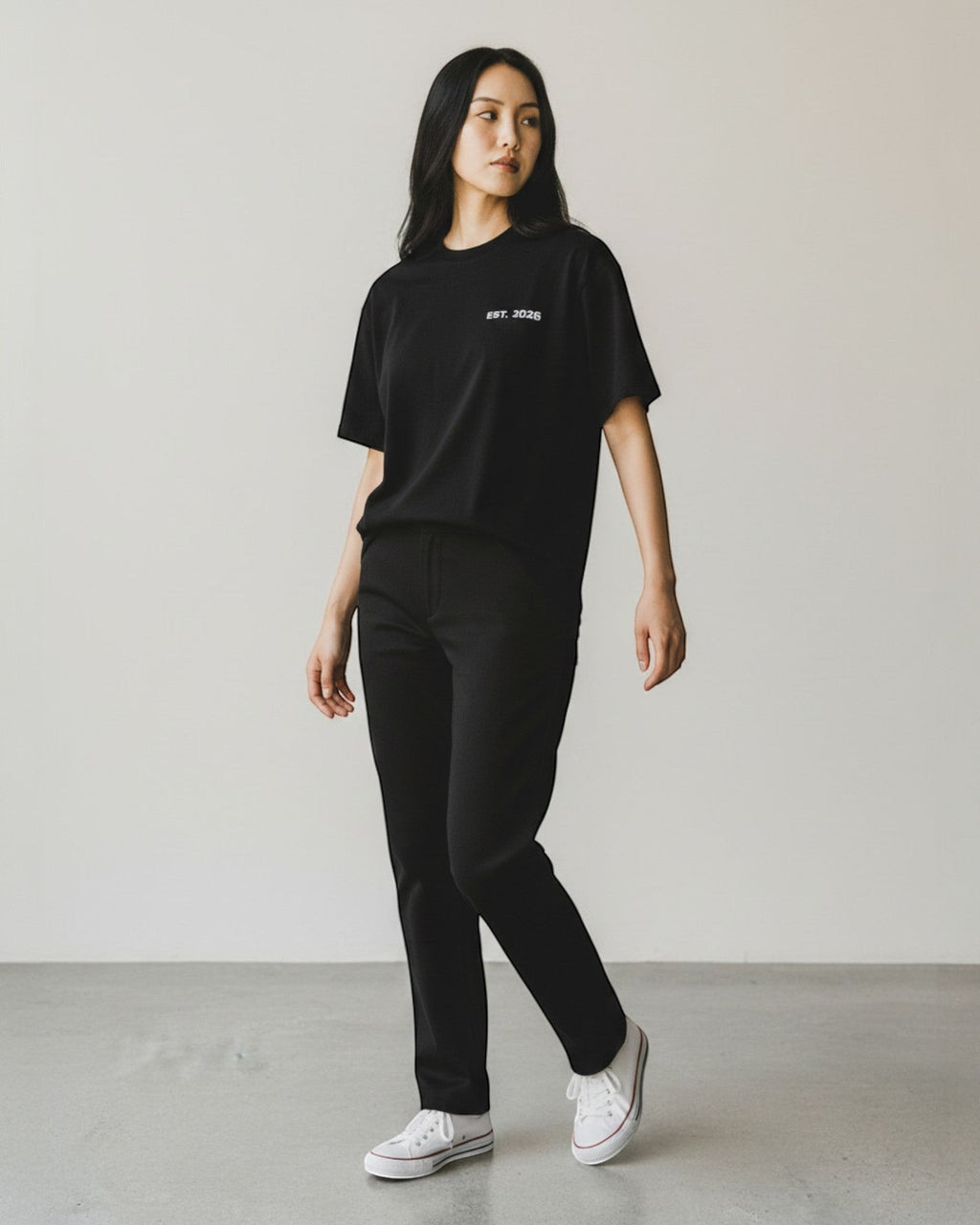 FALLR wear black 100% cotton oversized t-shirt with minimalist graphic print and relaxed fit, worn by a woman with black pants and white sneakers.