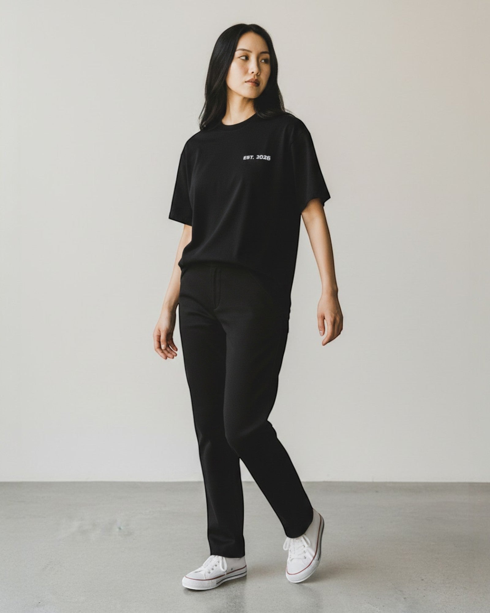 FALLR wear black 100% cotton oversized t-shirt with minimalist graphic print and relaxed fit, worn by a woman with black pants and white sneakers.