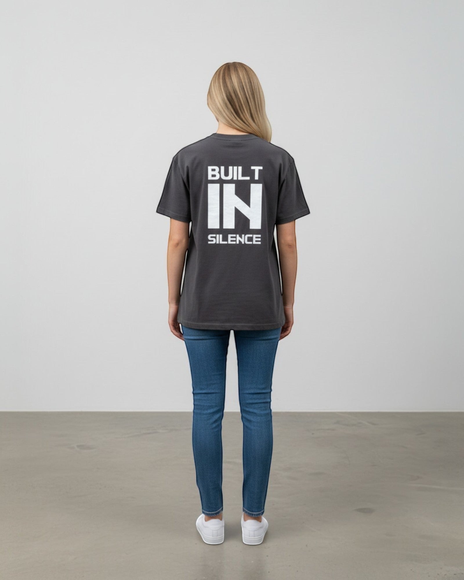 FALLR wear dark grey 100% cotton oversized t-shirt with white "BUILT IN SILENCE" graphic print on back, worn by a woman.