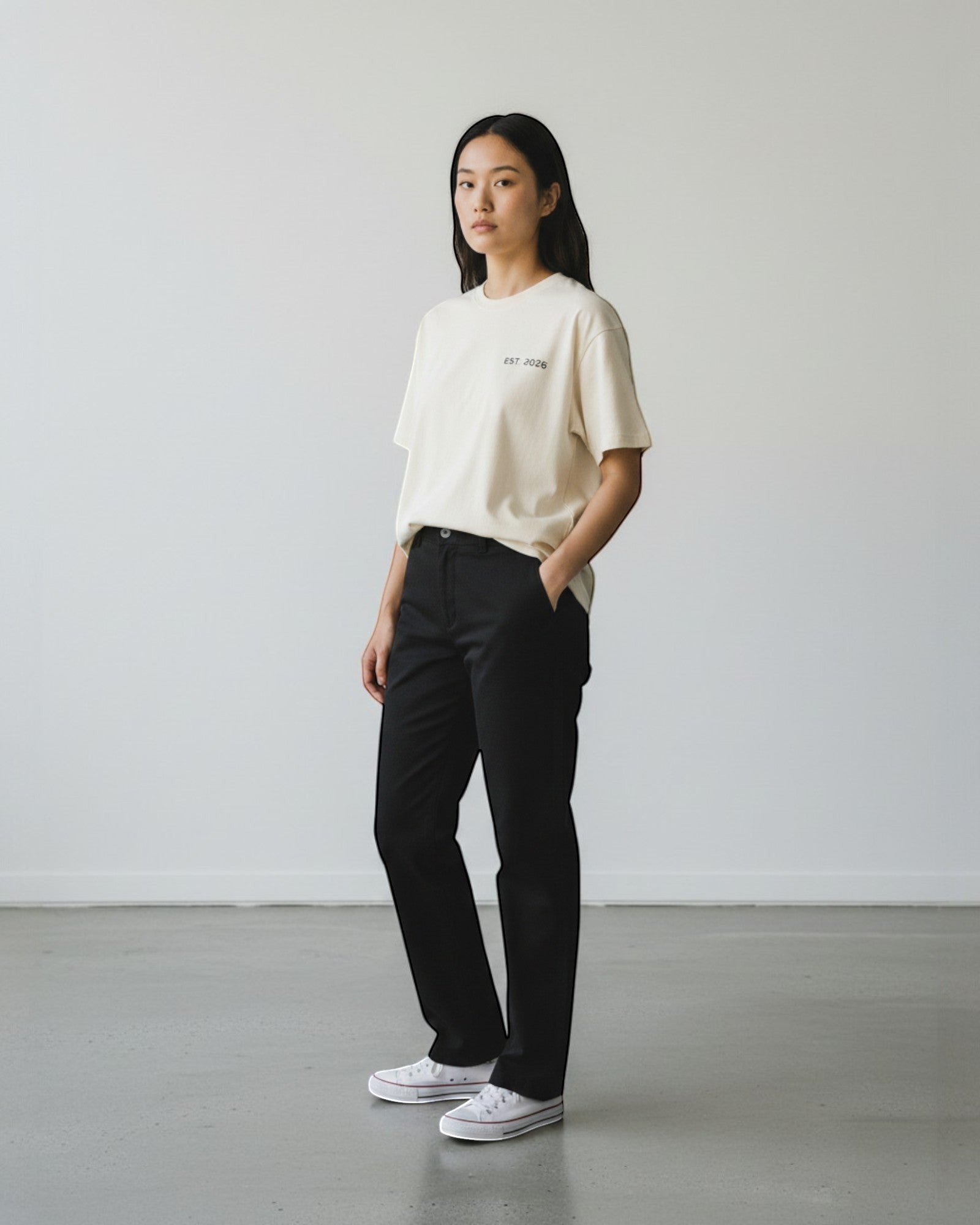 FALLR wear cream 100% cotton oversized t-shirt with minimal 'EST 2026' graphic print on chest. Model wears black trousers and white sneakers.