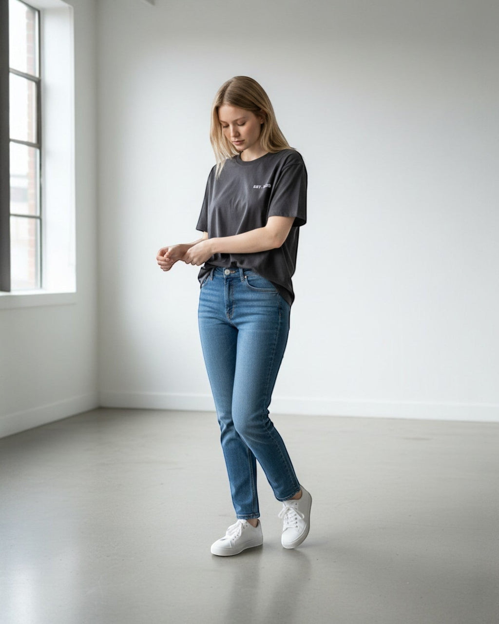 FALLR wear dark grey 100% cotton oversized t-shirt with a subtle white graphic print on the chest, worn by a woman with blue jeans and white sneakers.