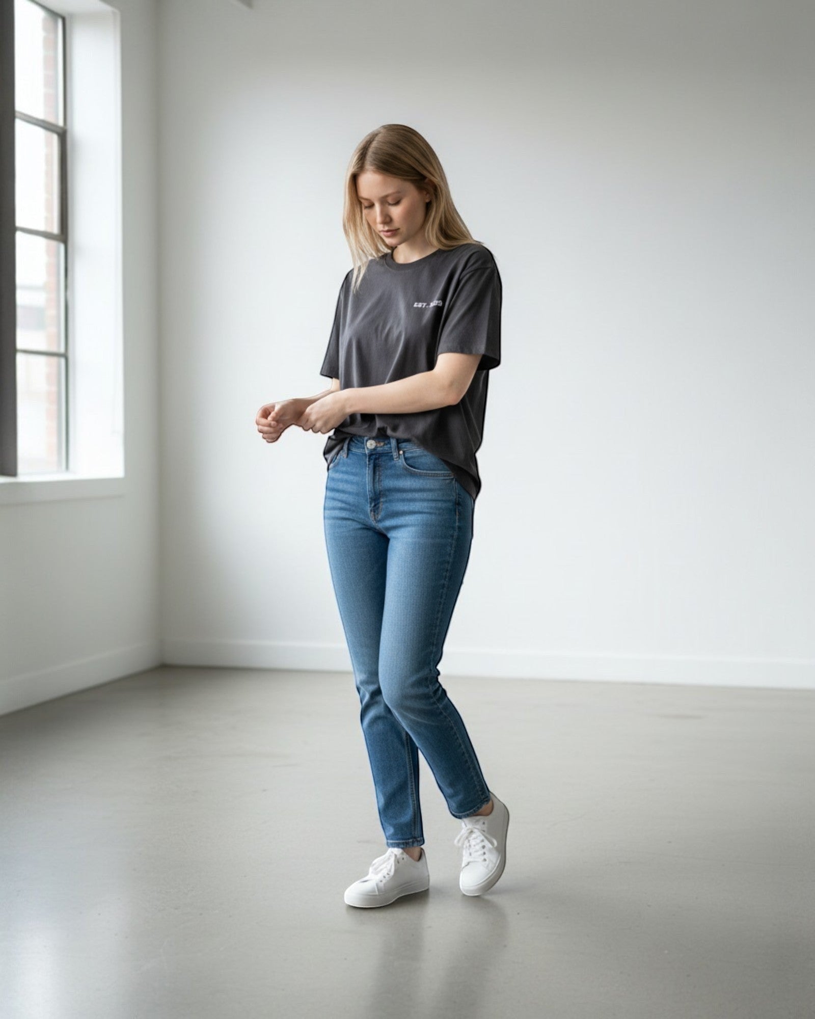 FALLR wear dark grey 100% cotton oversized t-shirt with a subtle white graphic print on the chest, worn by a woman with blue jeans and white sneakers.