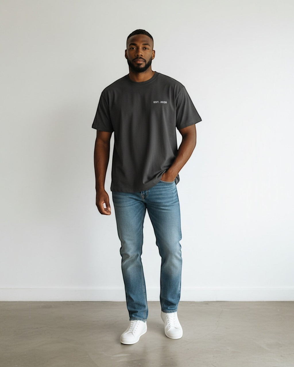 FALLR wear dark grey 100% cotton oversized t-shirt with "EST. 2026" graphic, worn by a man in blue jeans and white sneakers.
