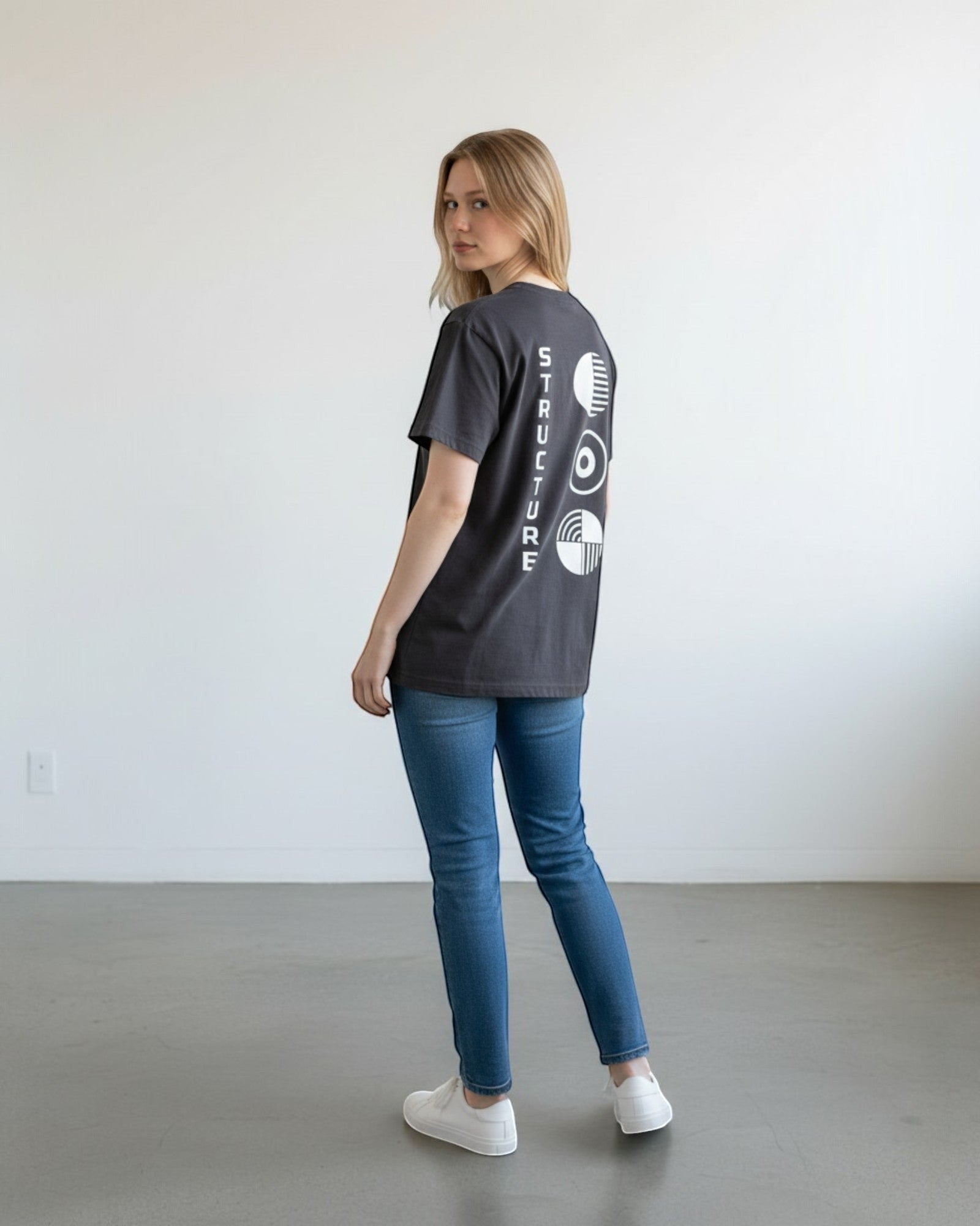 FALLR wear dark grey 100% cotton oversized t-shirt with white graphic print on back. Model is wearing jeans and white sneakers.