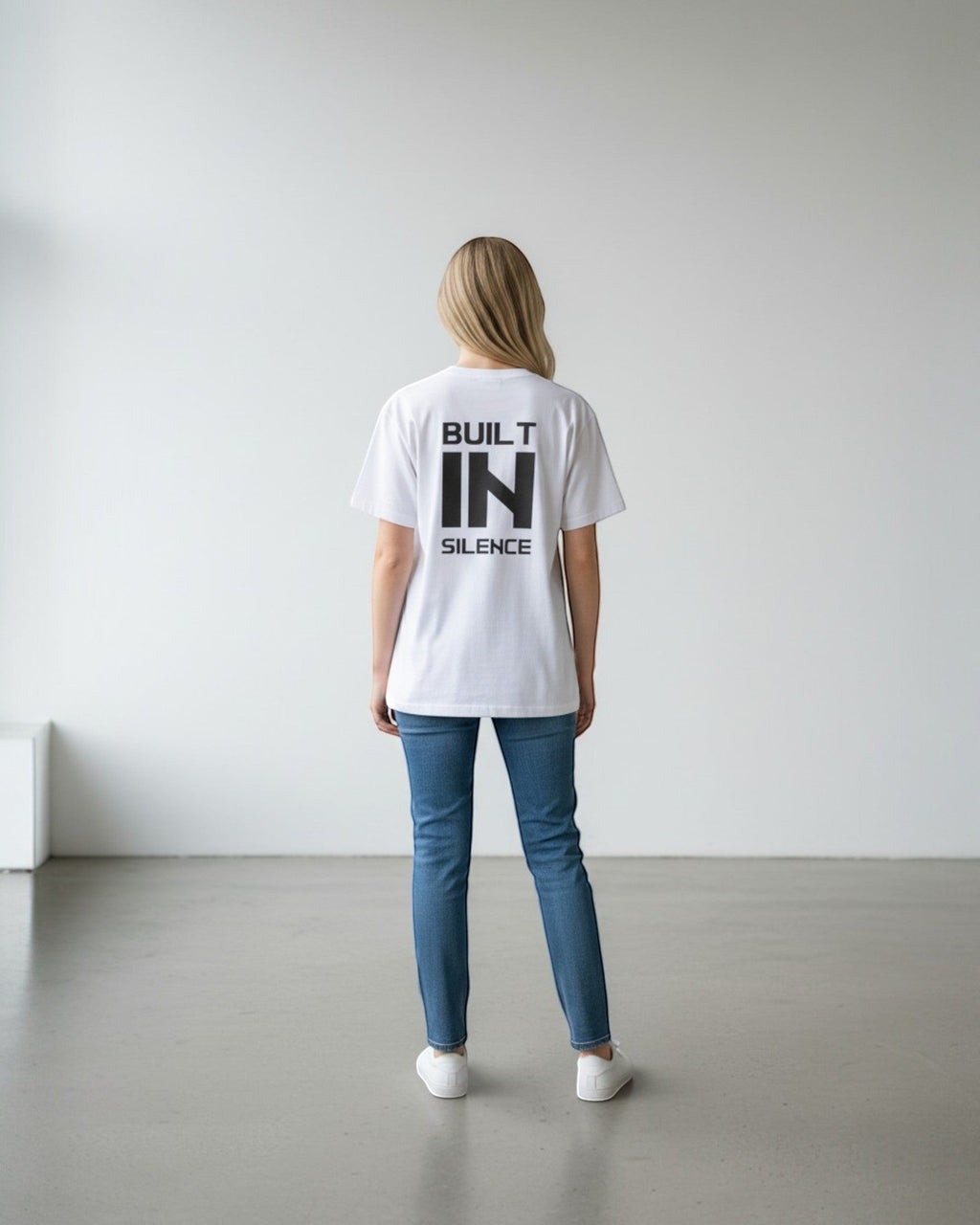 FALLR wear white 100% cotton oversized t-shirt with black "BUILT IN SILENCE" graphic print on back, worn by a woman.