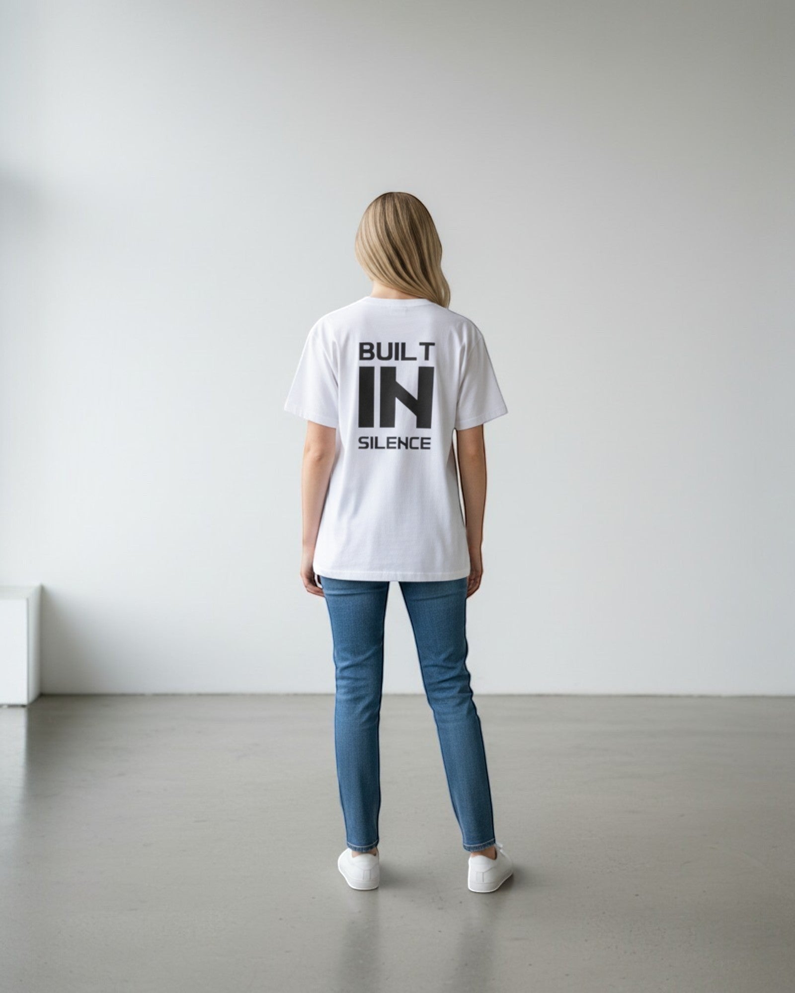 FALLR wear white 100% cotton oversized t-shirt with black "BUILT IN SILENCE" graphic print on back, worn by a woman.