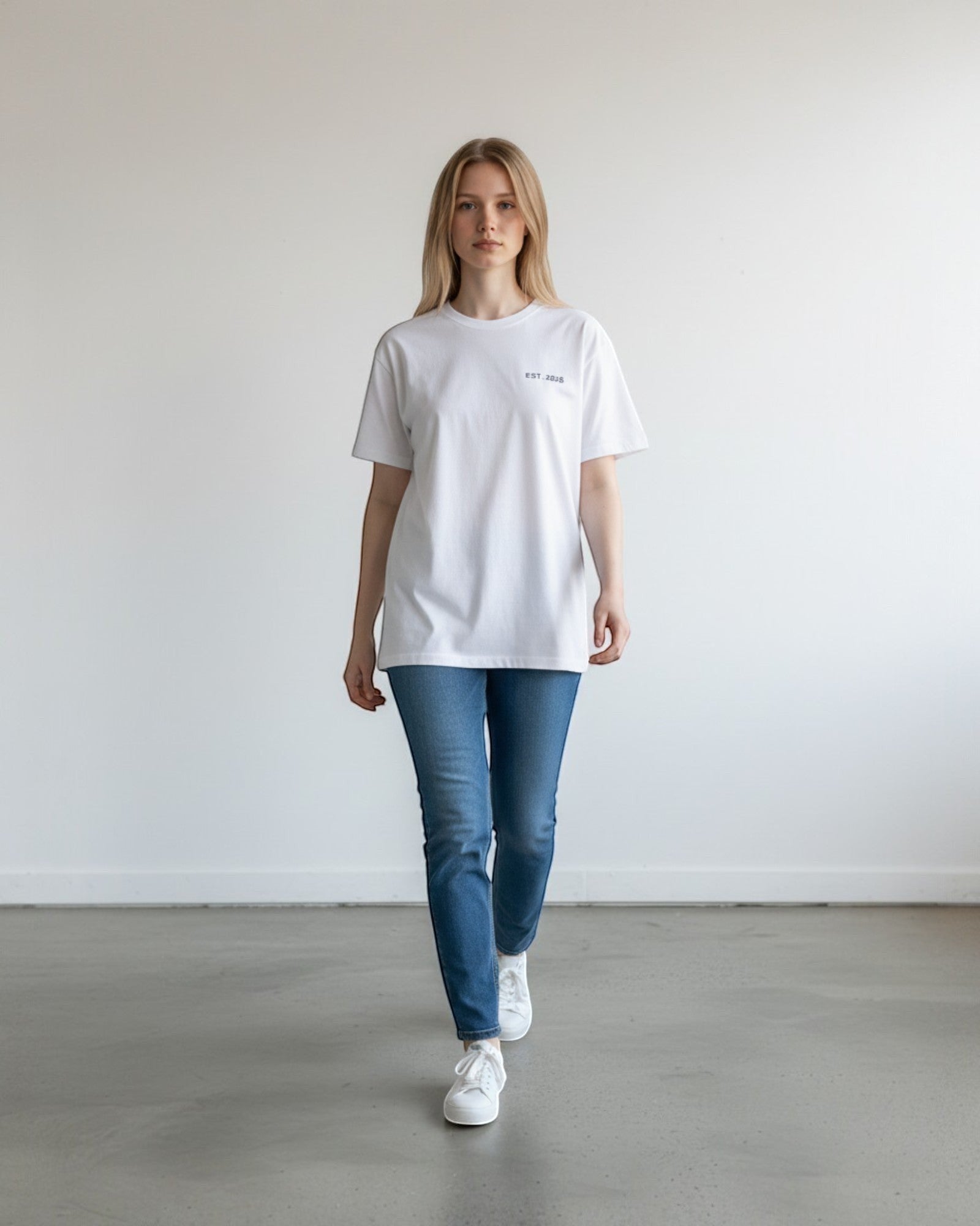 FALLR wear white 100% cotton oversized t-shirt with small navy graphic print on chest, worn by a woman with blue jeans.