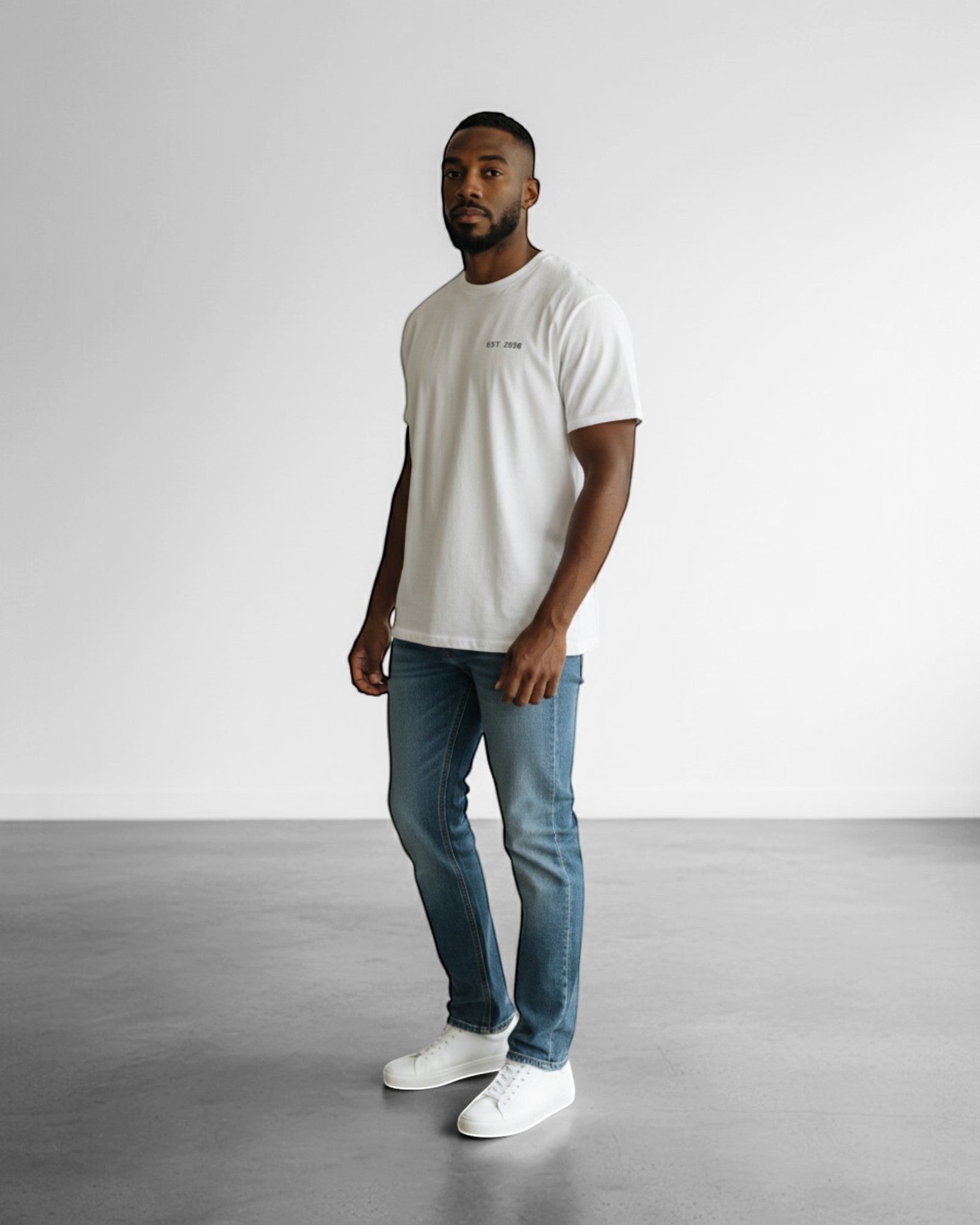 FALLR wear white 100% cotton oversized tee with subtle graphic print, worn by a man with blue jeans and white sneakers.